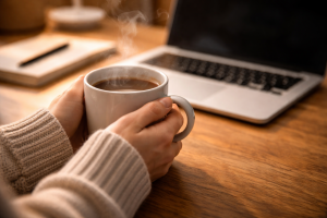 9210226 Hands holding a warm mug near a laptop, creating a vivid, sensory scene.